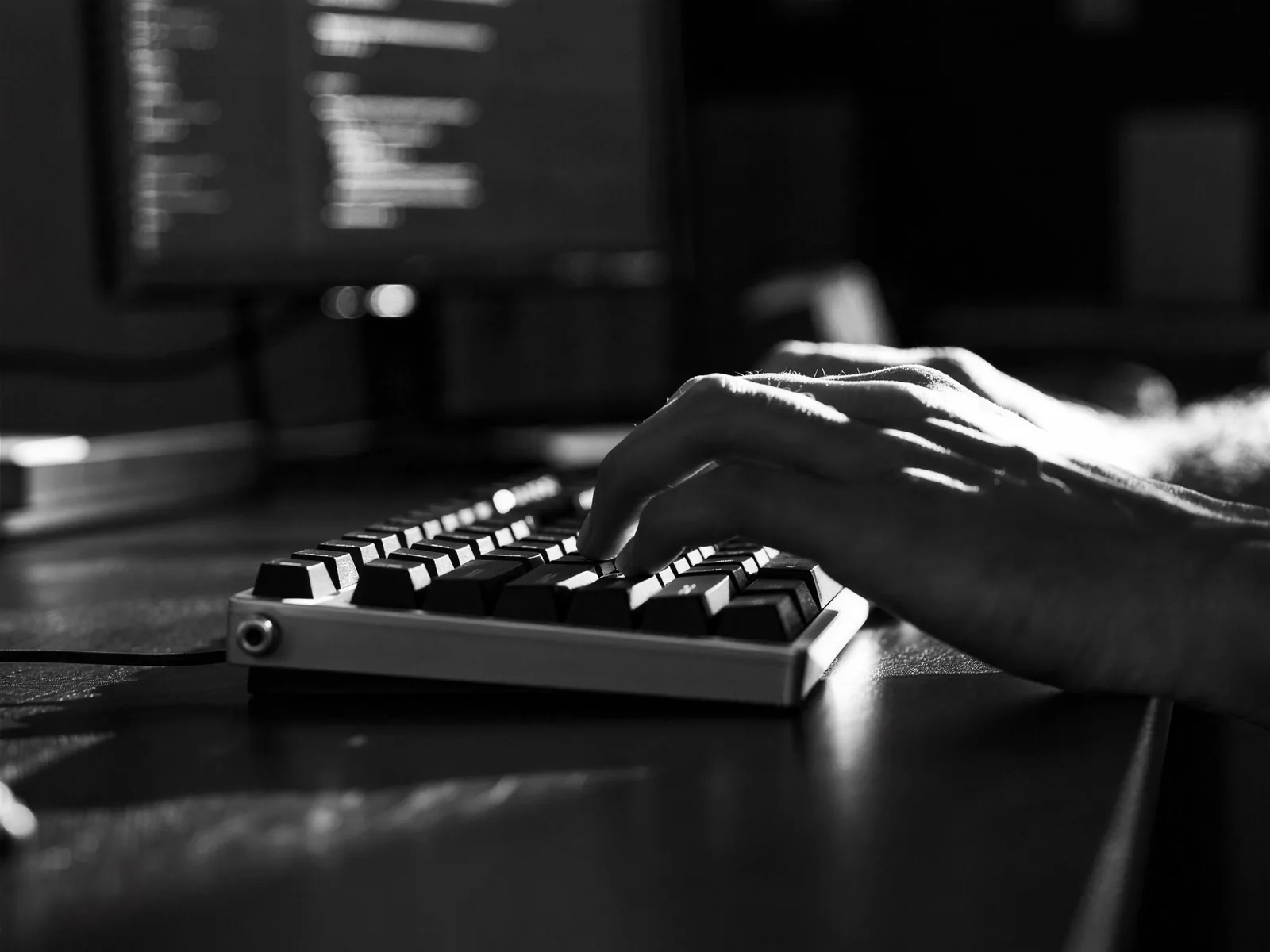 Hands typing on a mechanical keyboard in low, raking light